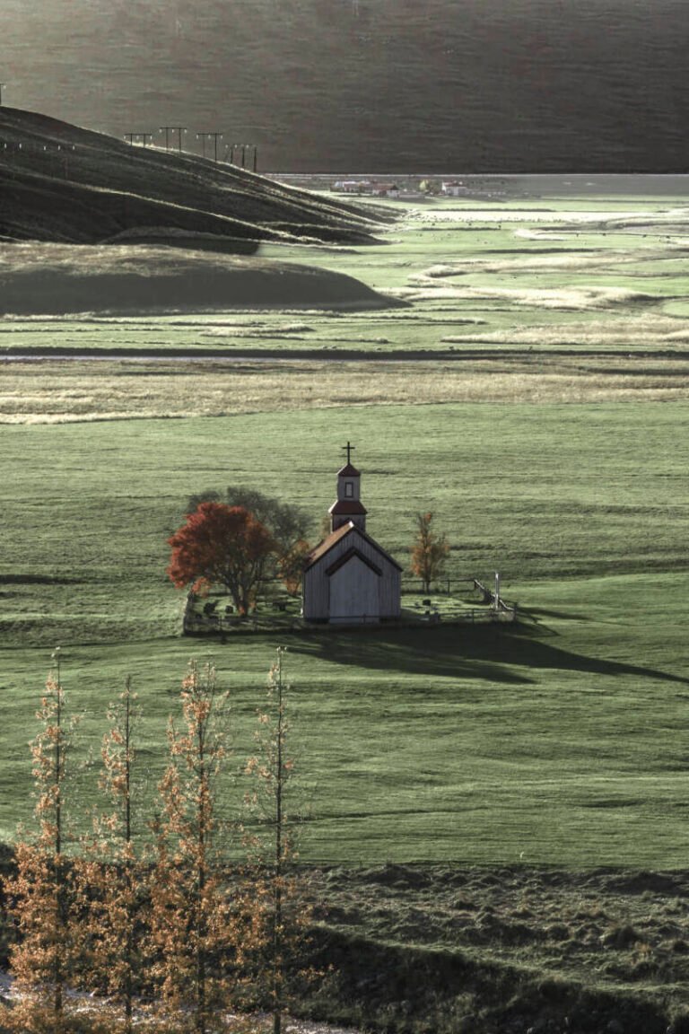 Vertical view of a small chapel on a green valley with a row of autumn poplars in the foreground