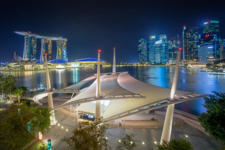 Marina Bay Sands and Singapore skyline lit at blue hour, with a white tensile canopy structure beside the calm bay.